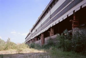 Veduta da nord ovest dei capannoni dell’acciaieria Vitali prima dello smantellamento; in primo piano, il muro dell’ex parco rottami. Fotografia di Filippo Gallino per Settore Riassetto Urbano, Città di Torino, giugno 2001.
